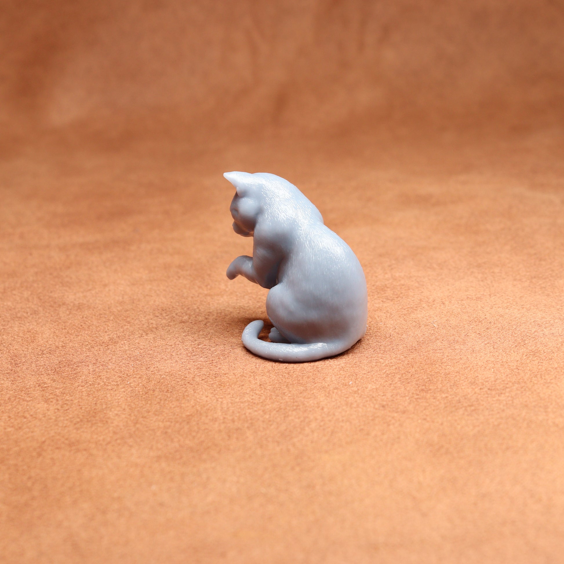 grey resin miniature cat examining its paw on a brown background