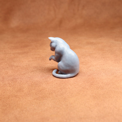 grey resin miniature cat examining its paw on a brown background