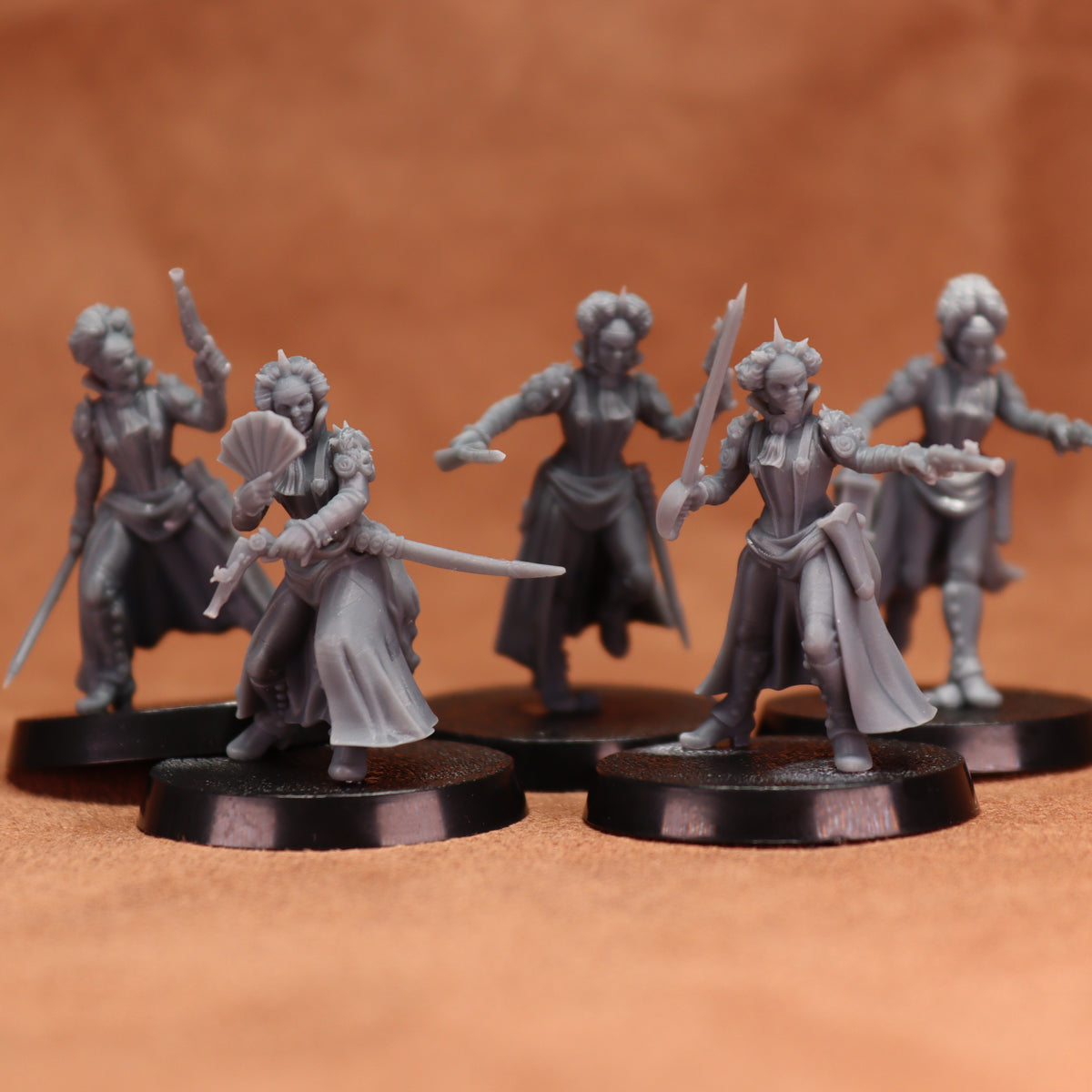 Five unpainted gray fantasy miniature figurines posed on round black bases against a warm brown studio background.