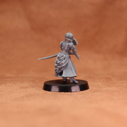 A small unpainted gray fantasy miniature figurine of a female warrior holding a sword, standing on a round black base against a warm brown textured background.