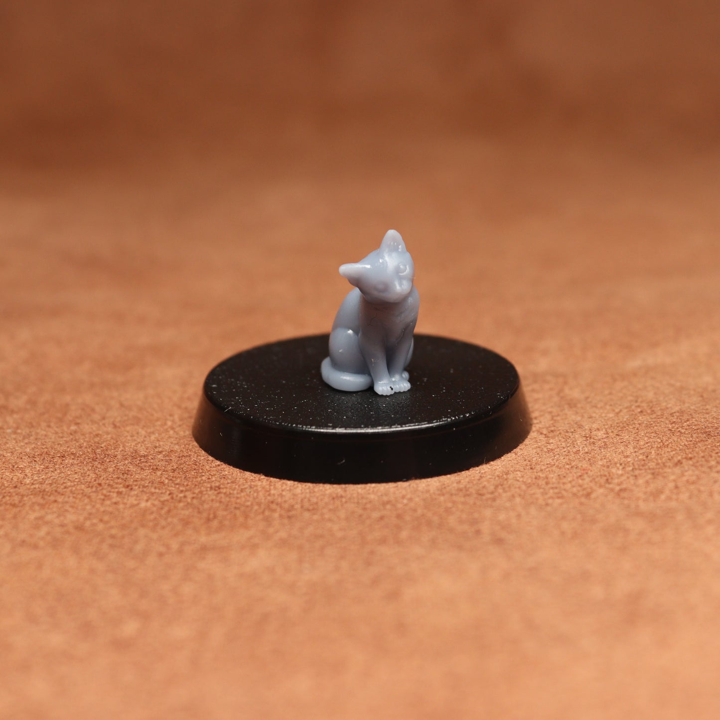 Small white cat figurine on a black round base against a brown background