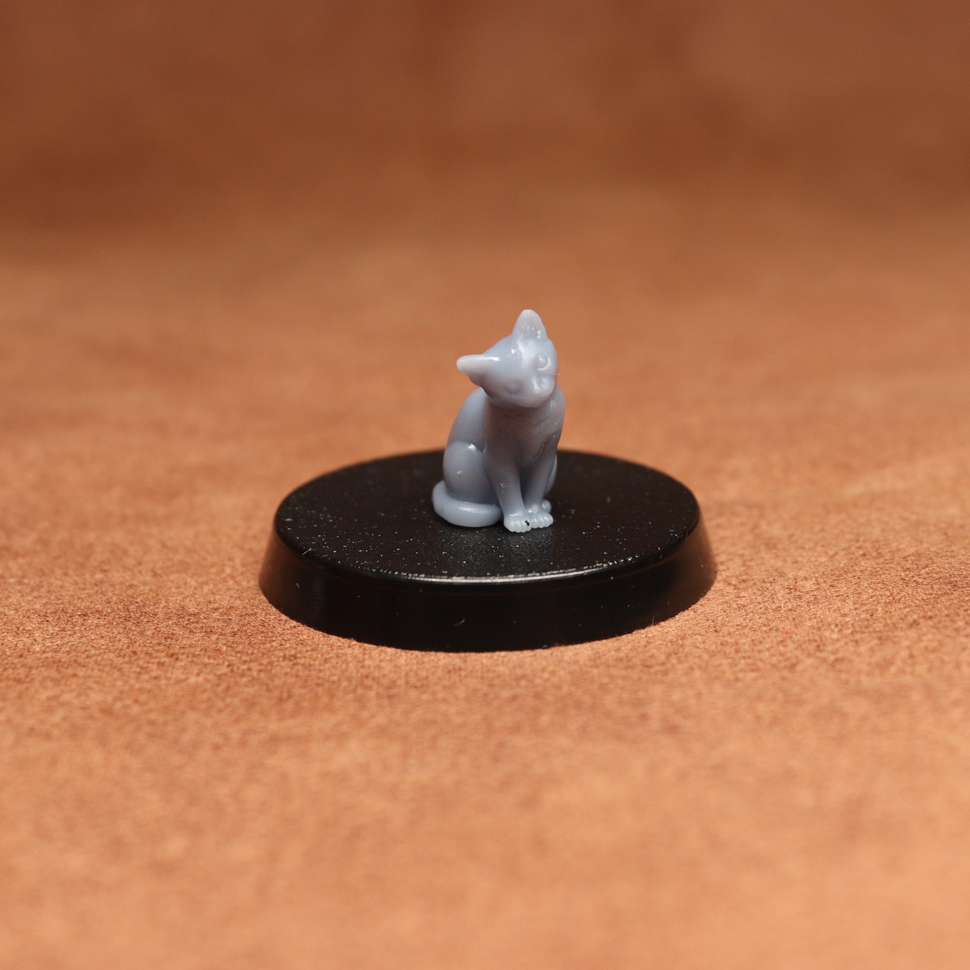 Small white cat figurine on a black round base against a brown background