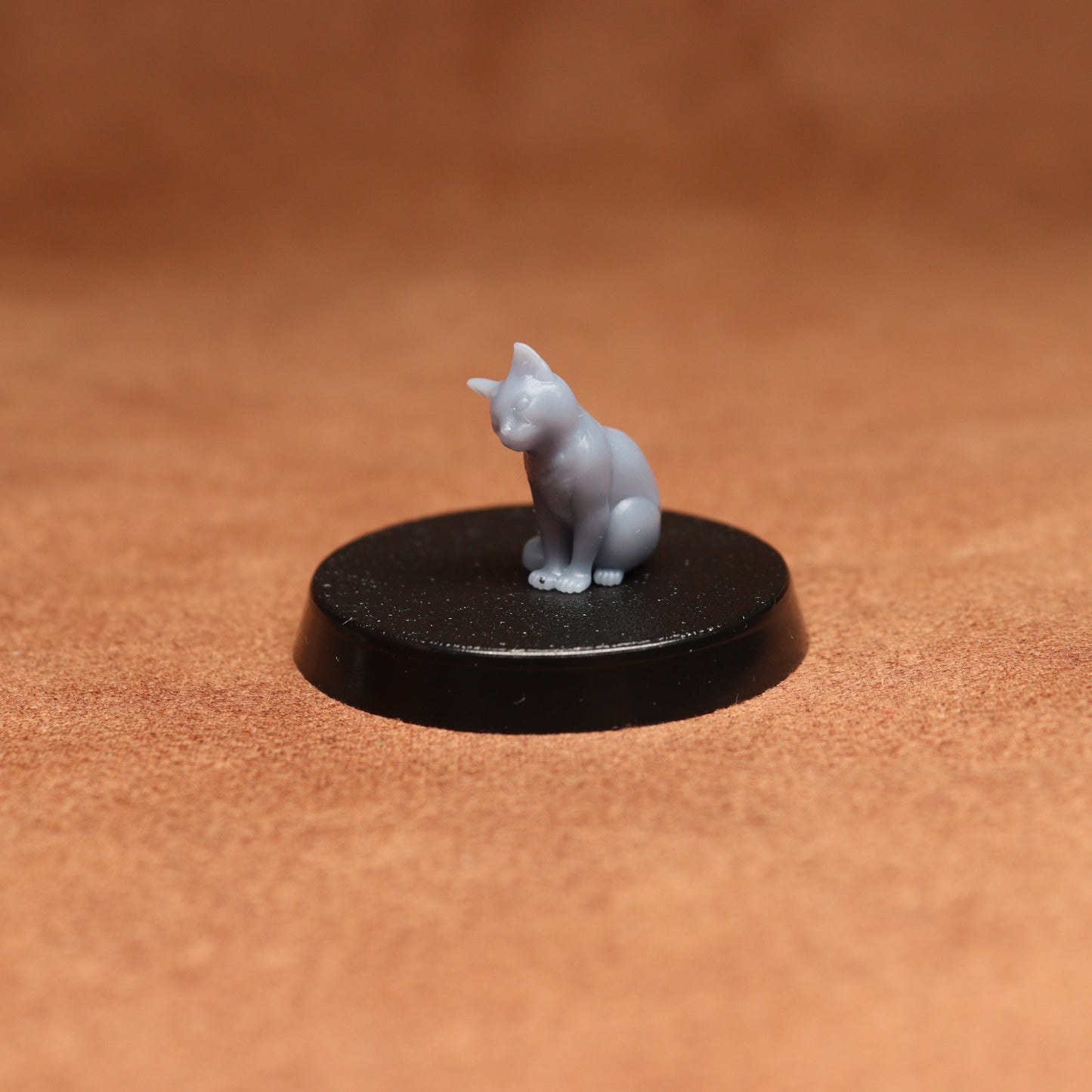 Small gray cat figurine on a black round base against a brown background