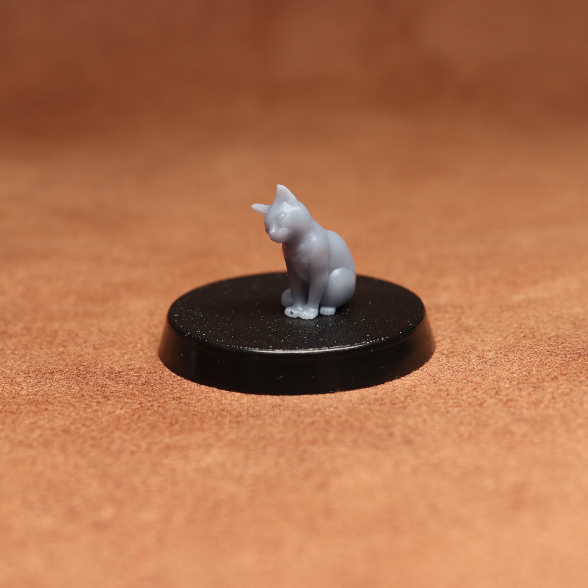 Small gray cat figurine on a black round base against a brown background