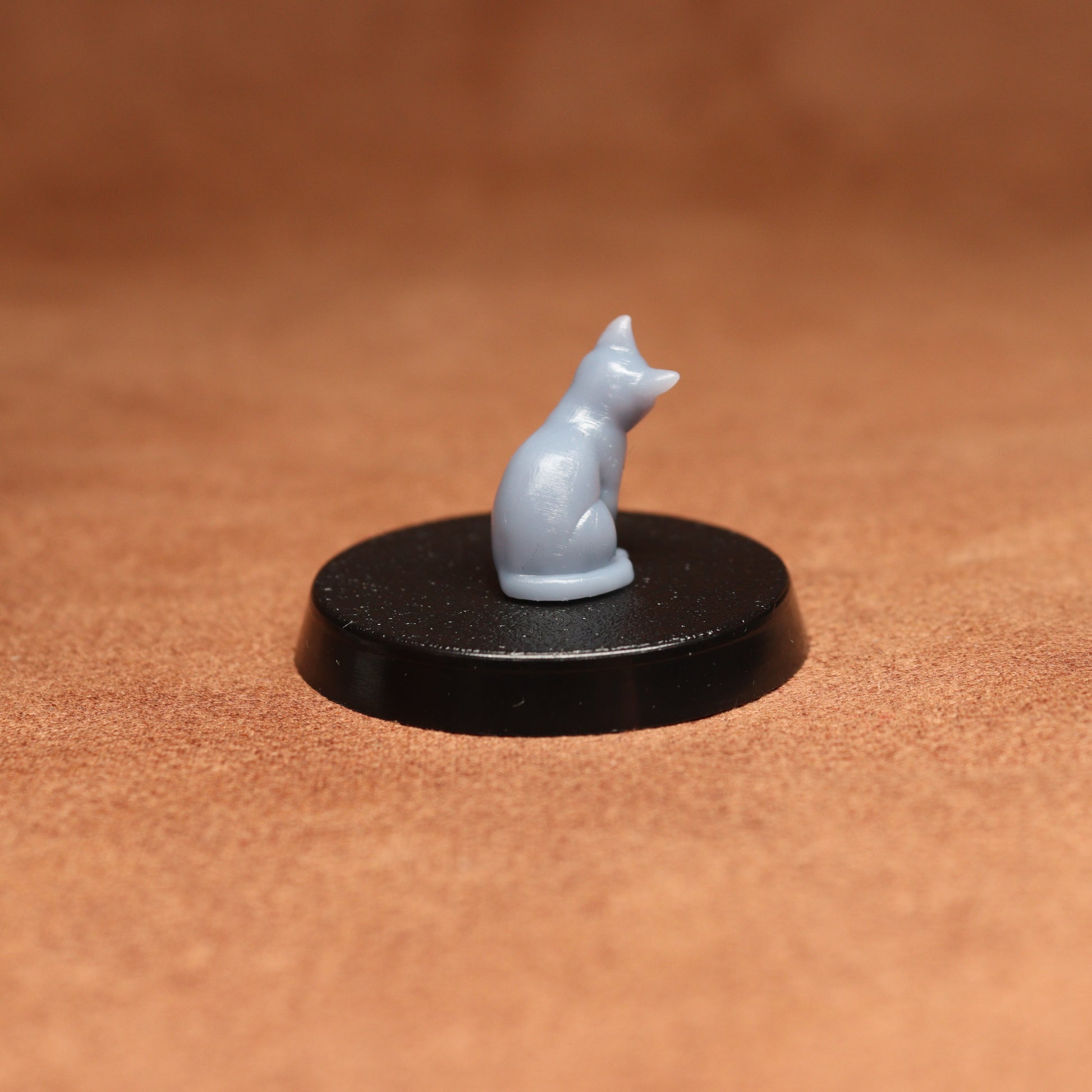 Small gray cat figurine on a black round base against a brown background