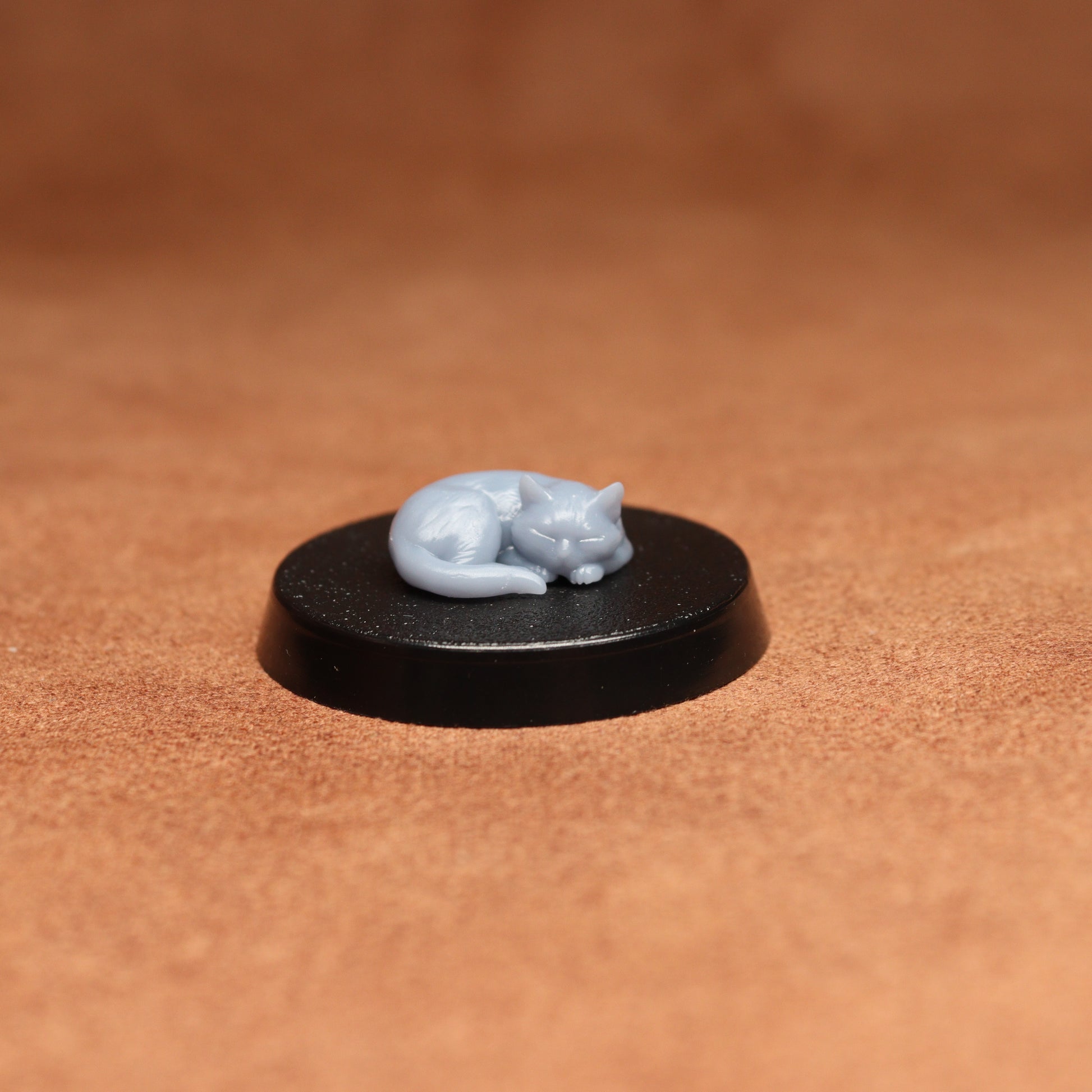 Small gray cat figurine on a black round base against a brown background