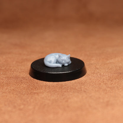 Small gray cat figurine on a black round base against a brown background