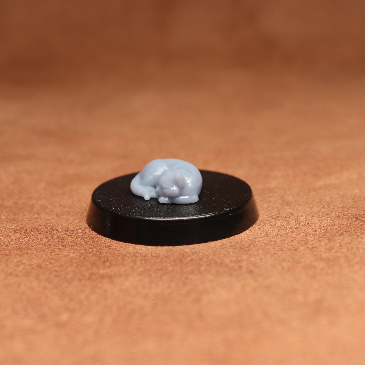 Small grey figurine on a black round base against a brown background