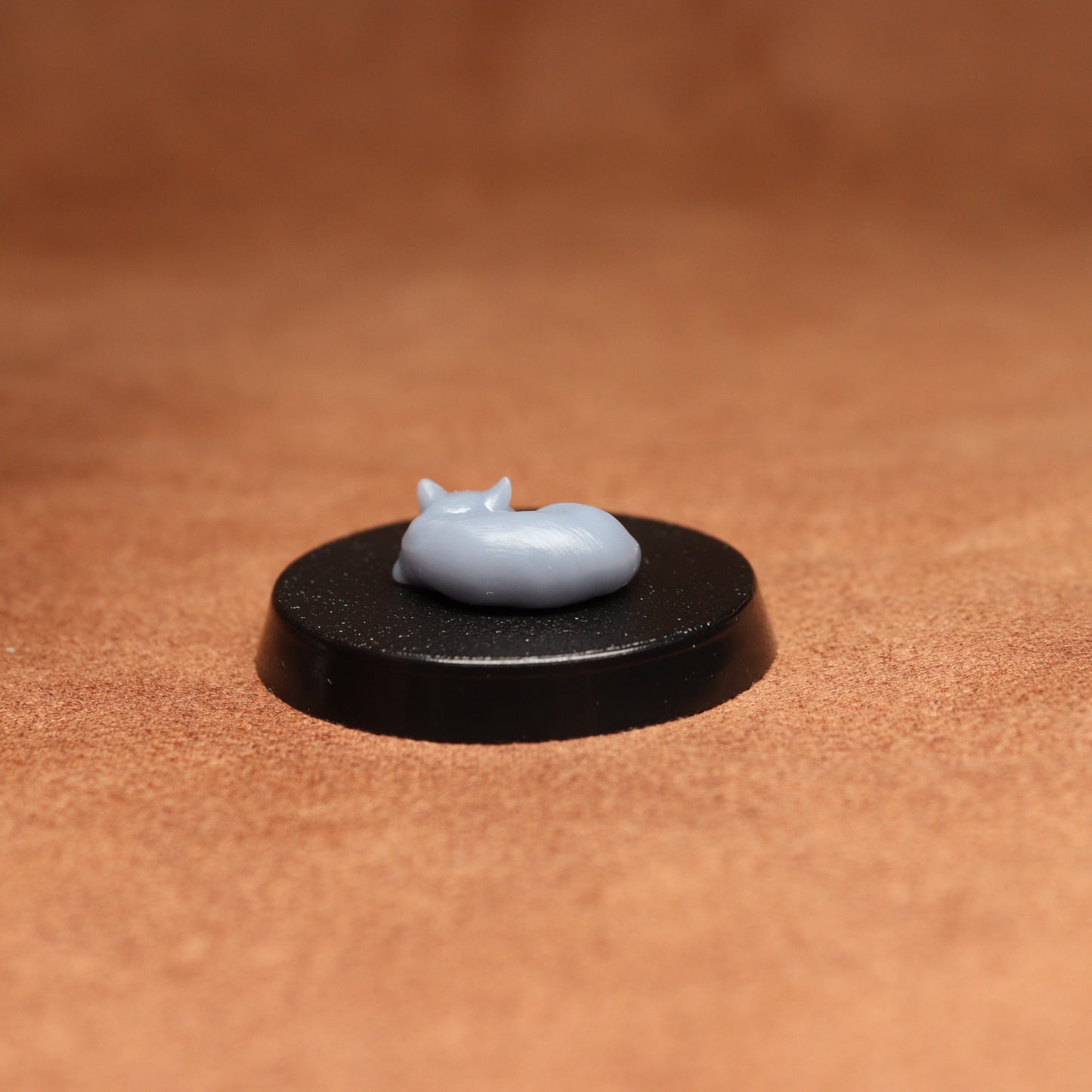 Small gray figurine on a black circular base against a brown background