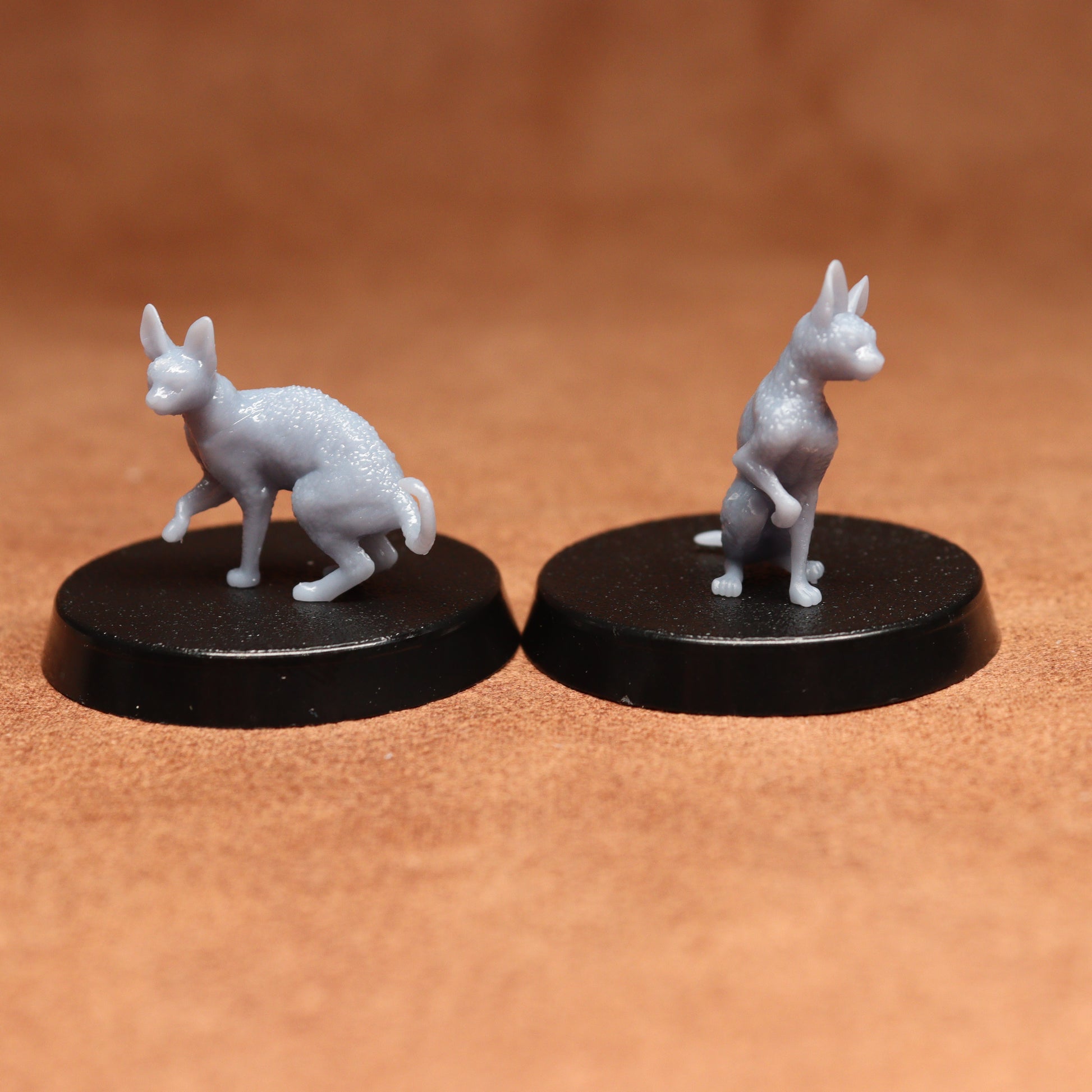 Two miniature cat figurines on black bases against a brown background