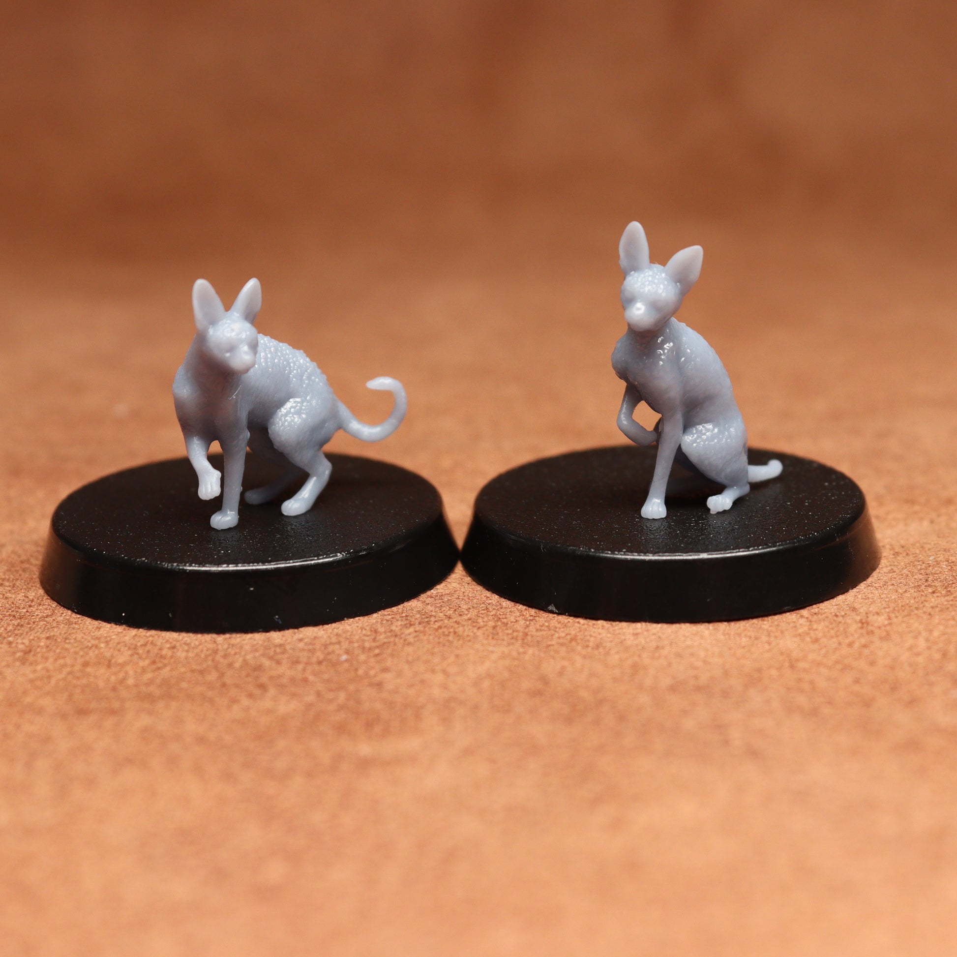 Two small white cat figurines on black bases against a brown background
