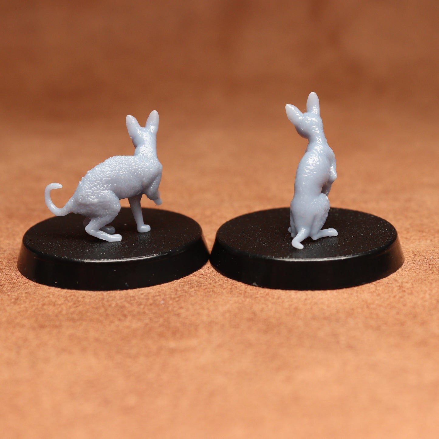 Two small white cat figurines on black bases against a brown background