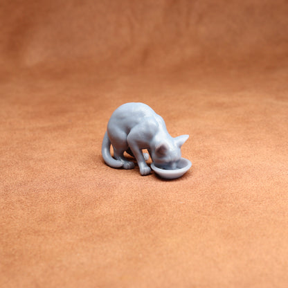 Gray cat figurine drinking from a bowl on a brown surface
