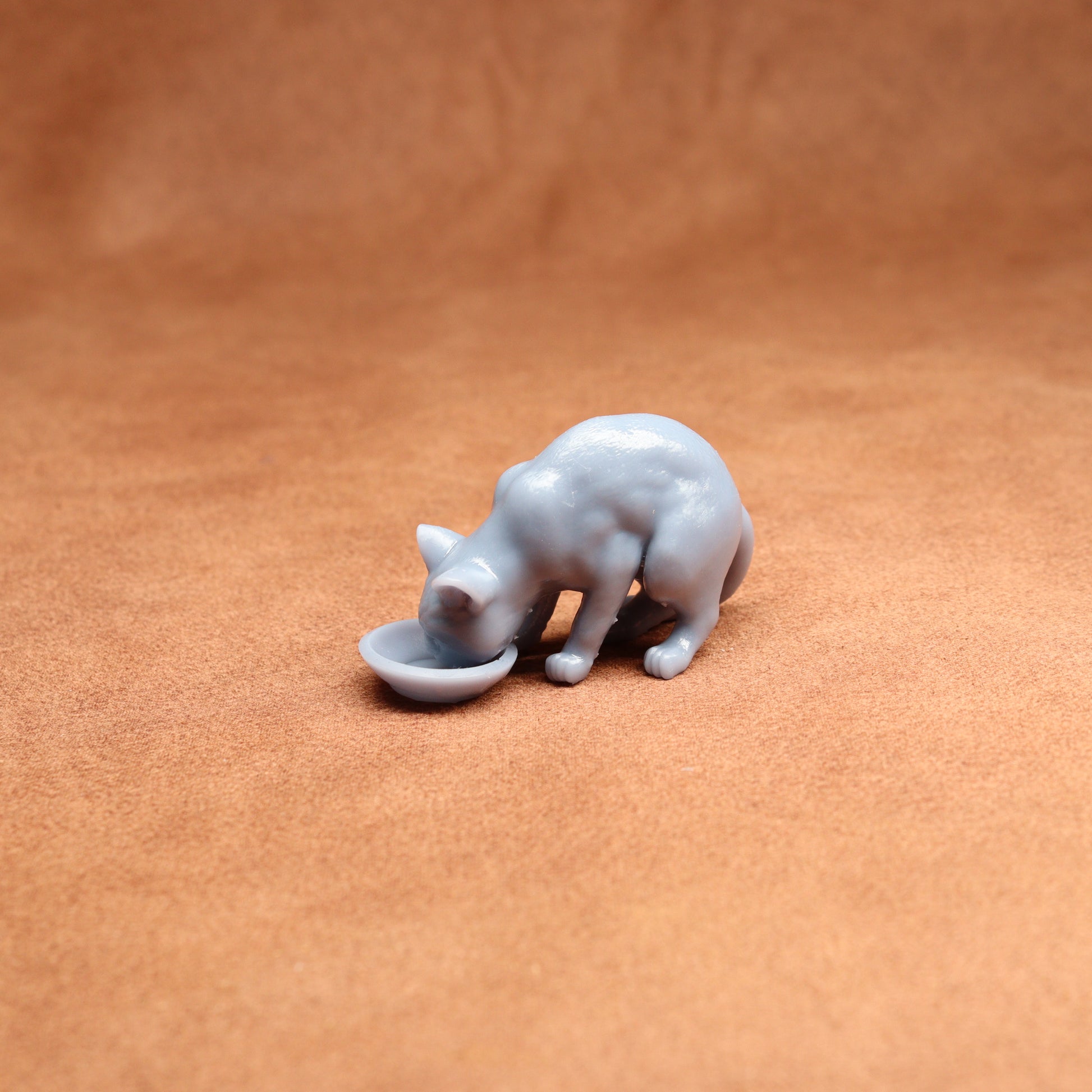 Small resin cat figurine drinking from a bowl on a brown surface