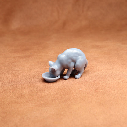 Small resin cat figurine drinking from a bowl on a brown surface