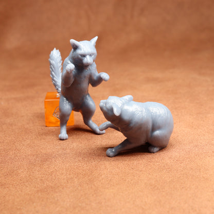 Two gray cat figurines on a brown surface with an orange dice in the background.