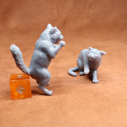 Two grey cat figurines on a brown surface with an orange dice in the background.