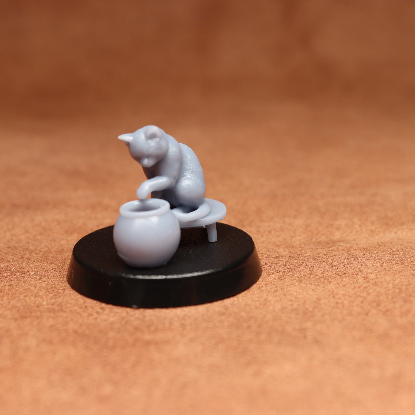grey resin miniature cat figure on a black base with a brown background