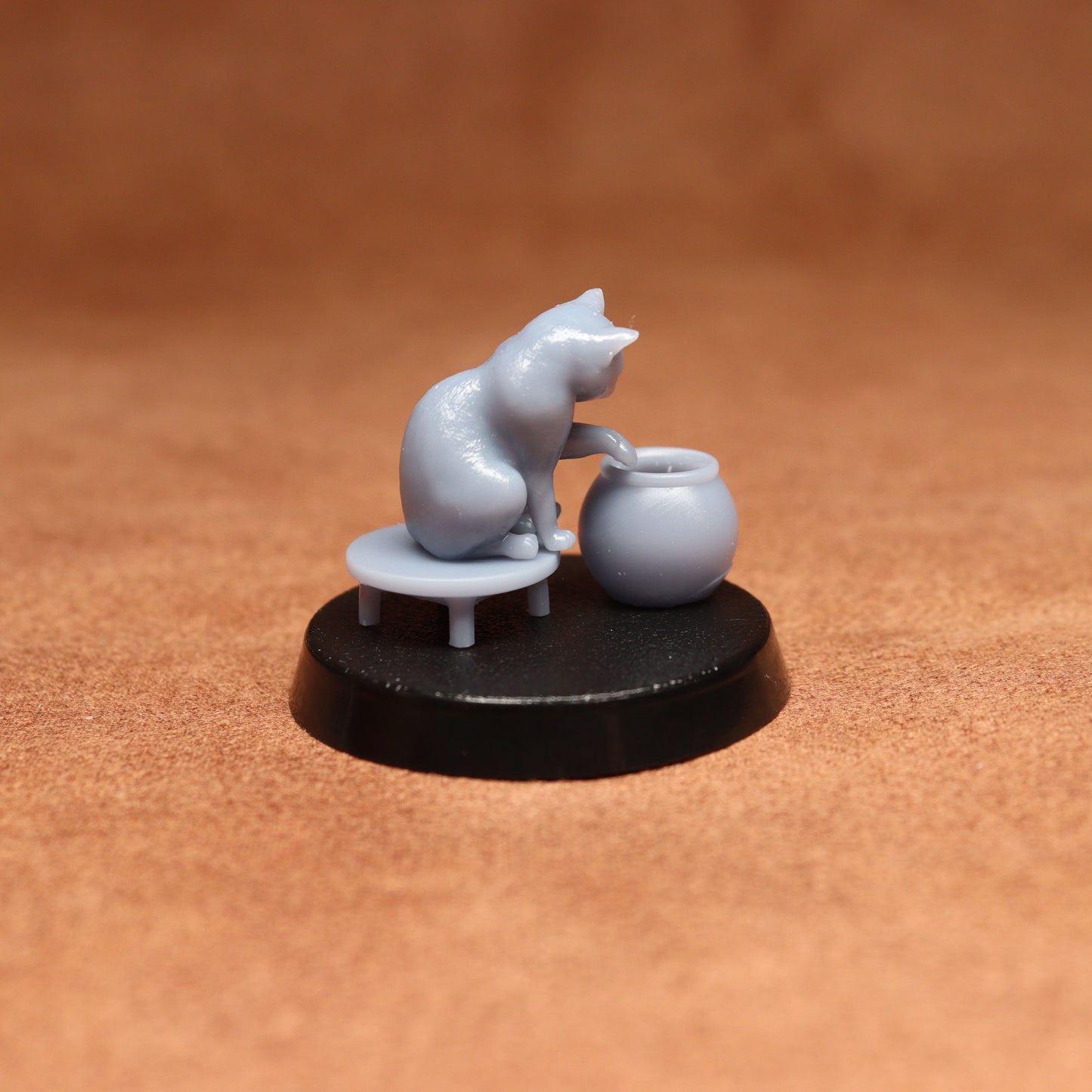 grey resin miniature cat figure on a black base with a brown background