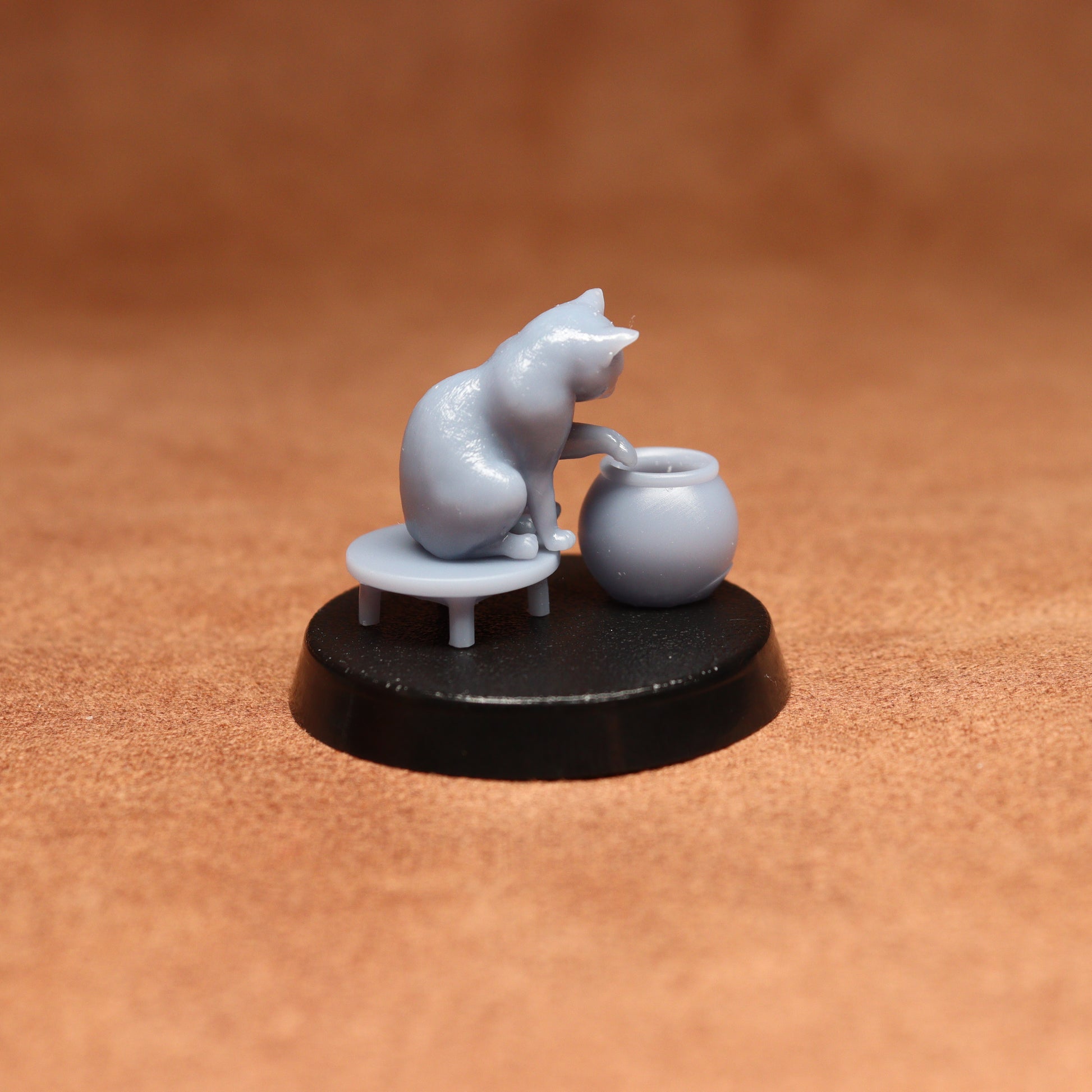 grey resin miniature cat figure on a black base with a brown background