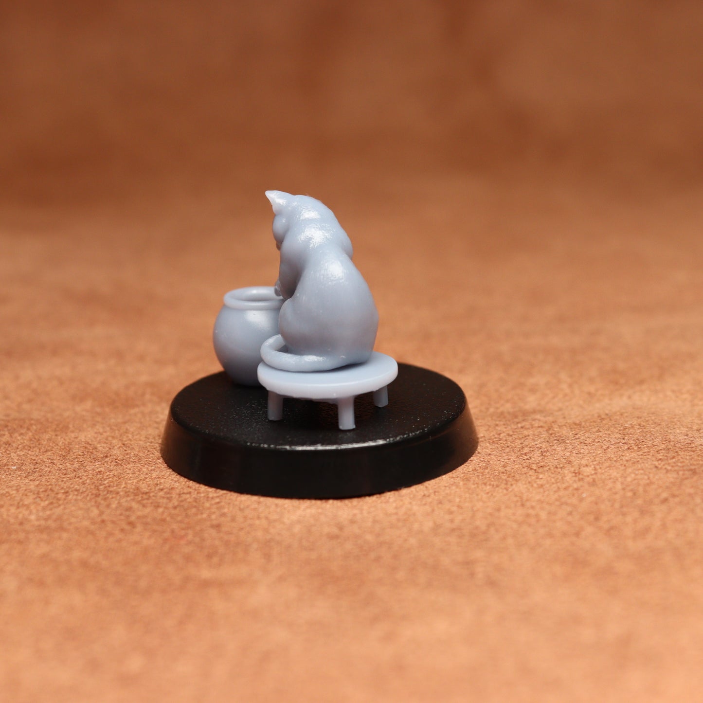 grey resin miniature cat figure on a black base with a brown background