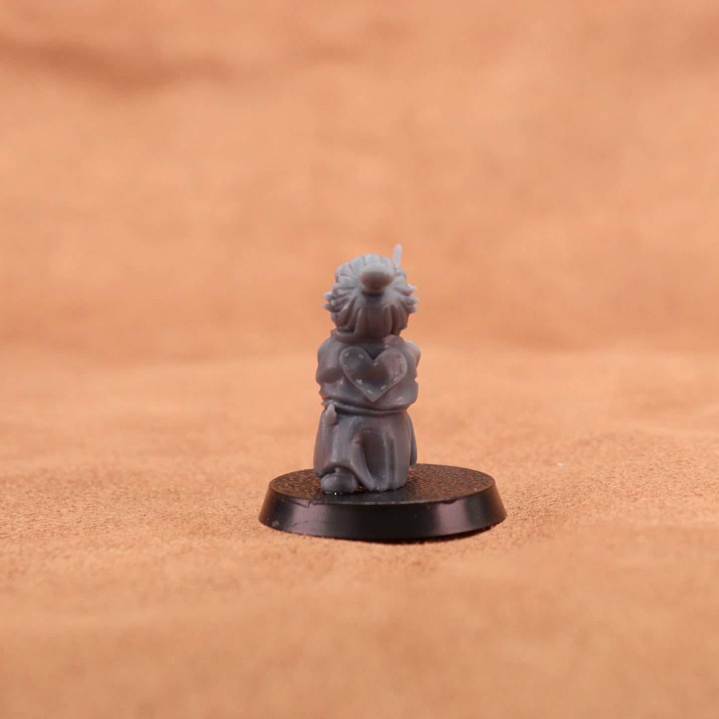 A small gray painted tabletop miniature figurine of a frog-like character in a samurai outfit holding a sword, mounted on a round black base. The background is a warm tan textured surface.