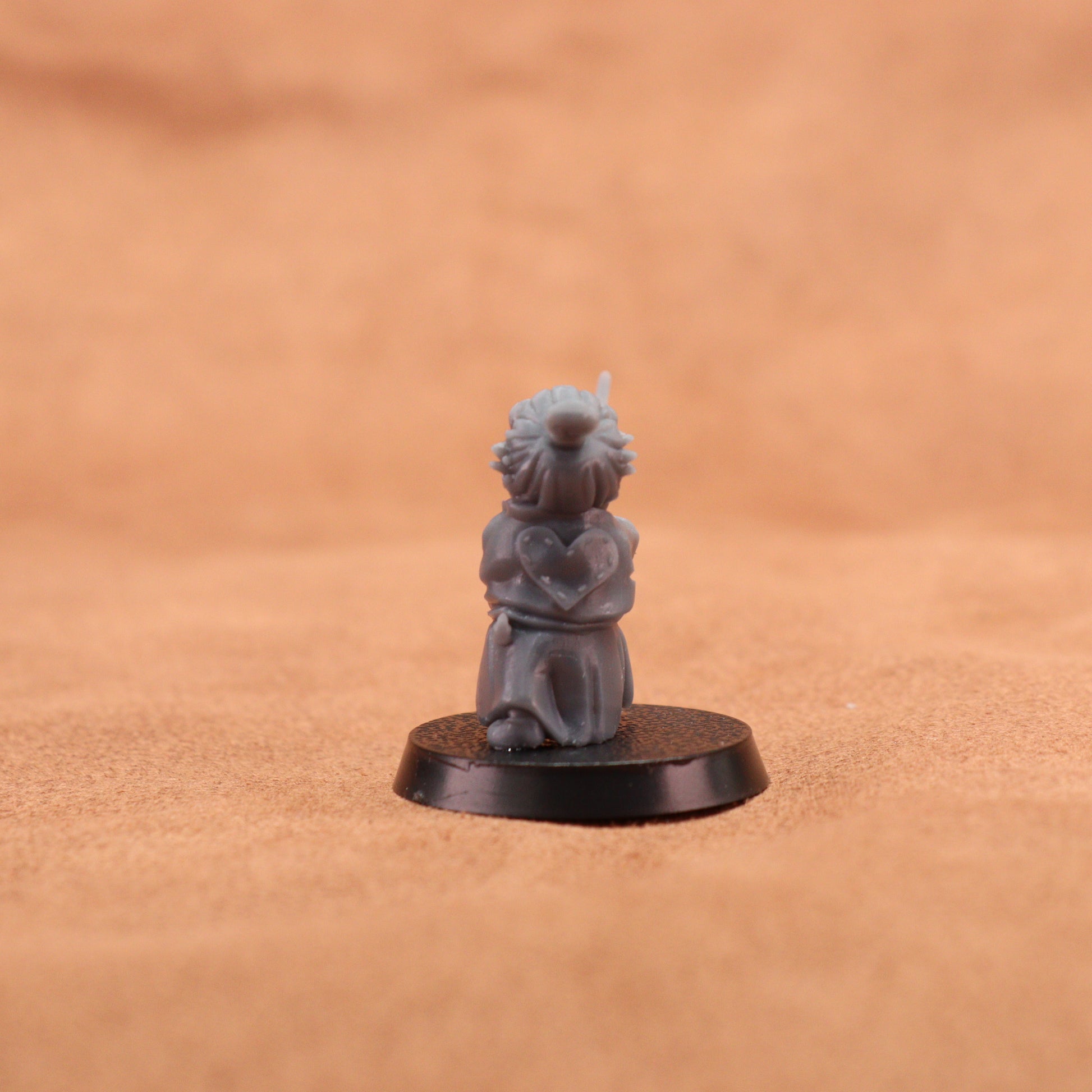 A small gray painted tabletop miniature figurine of a frog-like character in a samurai outfit holding a sword, mounted on a round black base. The background is a warm tan textured surface.