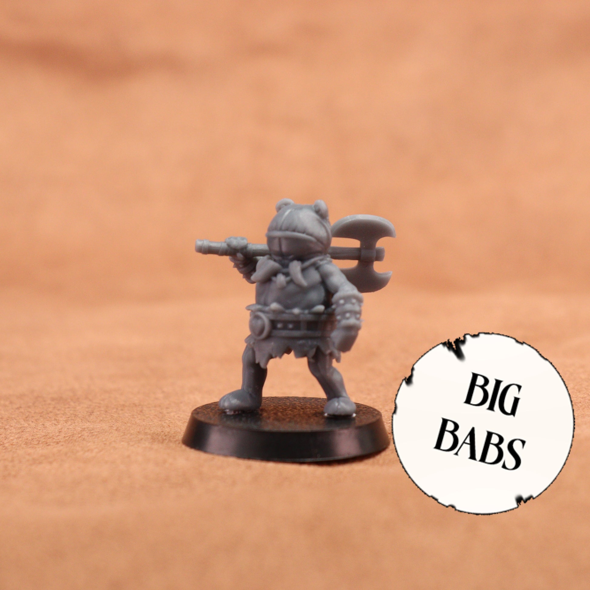A small gray fantasy warrior miniature figurine holding a double-headed axe, standing on a round black base against a warm tan background. A white circular badge with the text 'BIG BABS' appears in the lower right corner.