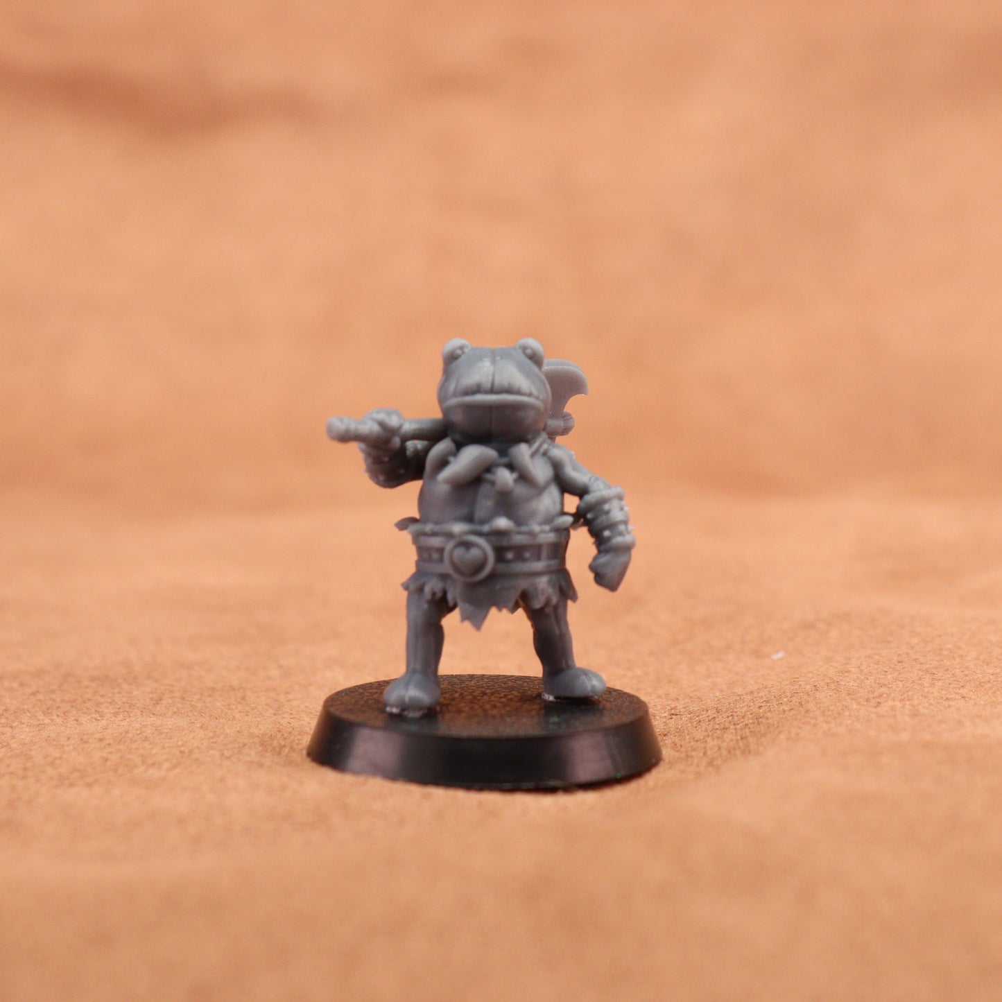 A small gray fantasy warrior miniature figurine holding a double-headed axe, standing on a round black base against a warm tan background.