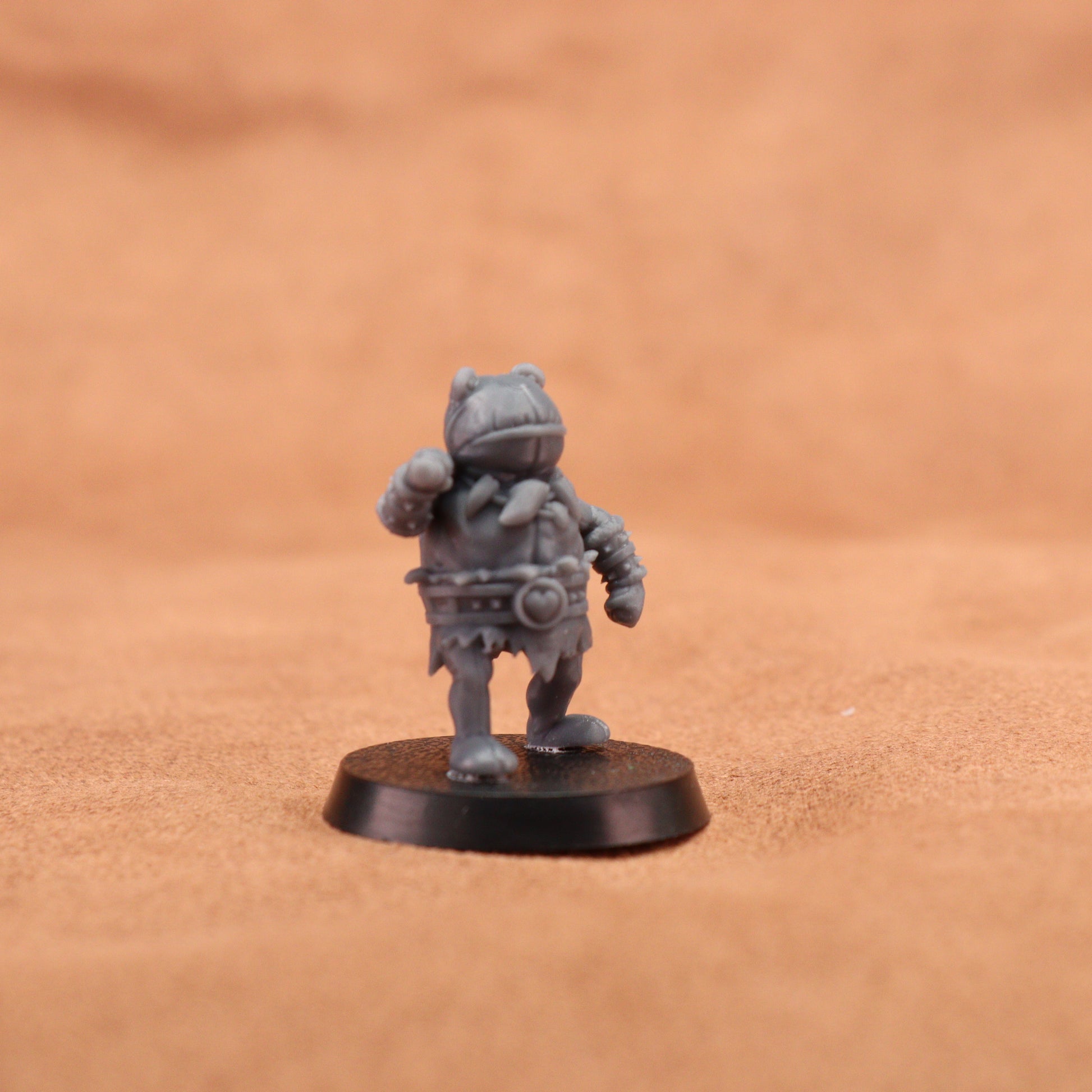 A small unpainted gray fantasy miniature figurine standing on a round black base, photographed against a warm brown textured background.