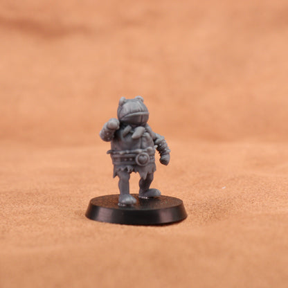 A small unpainted gray fantasy miniature figurine standing on a round black base, photographed against a warm brown textured background.