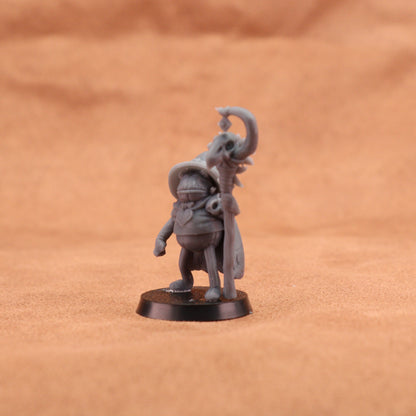 A small unpainted gray fantasy miniature figurine of a wizard holding a staff, standing on a round black base against a warm brown textured background.