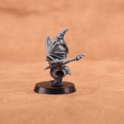 A small unpainted gray fantasy miniature figurine standing on a round black base, photographed against a warm tan textured background.