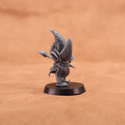 A small unpainted gray fantasy miniature figurine standing on a round black base, photographed against a warm tan textured background.