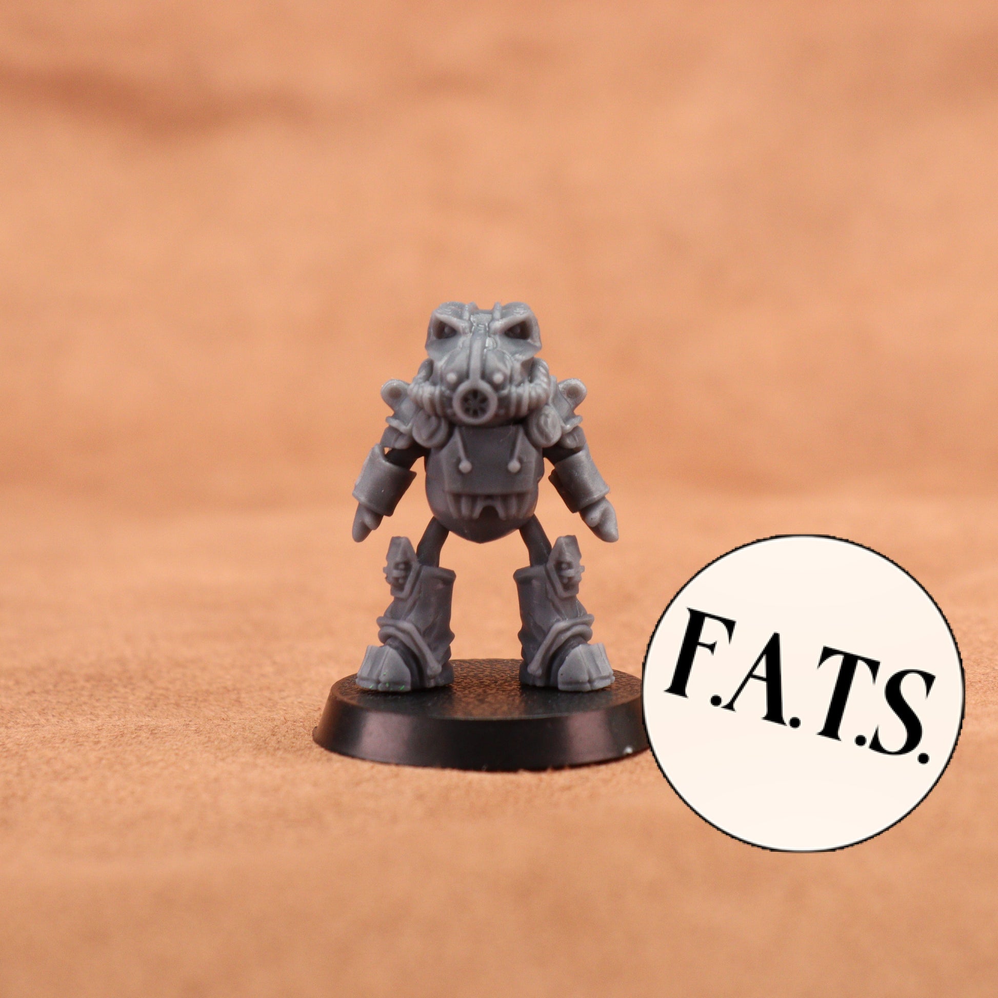 A small gray sci-fi miniature figurine standing on a round black base against a warm tan textured background, with a circular sticker reading “F.A.