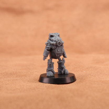 A small unpainted gray fantasy miniature figurine of a robotic or mechanical creature standing on a round black base, photographed against a warm tan textured background.
