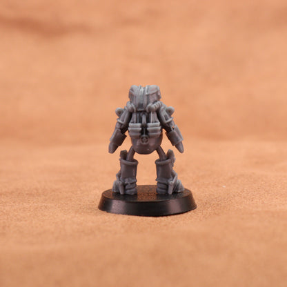 A small unpainted gray miniature figurine of a sci-fi robot or mecha standing on a round black base, photographed against a warm tan textured background.