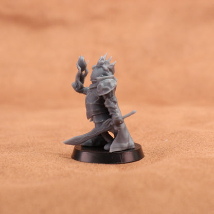 An unpainted gray fantasy miniature figurine of a crowned warrior holding a sword and staff, standing on a round black base against a warm brown textured background.