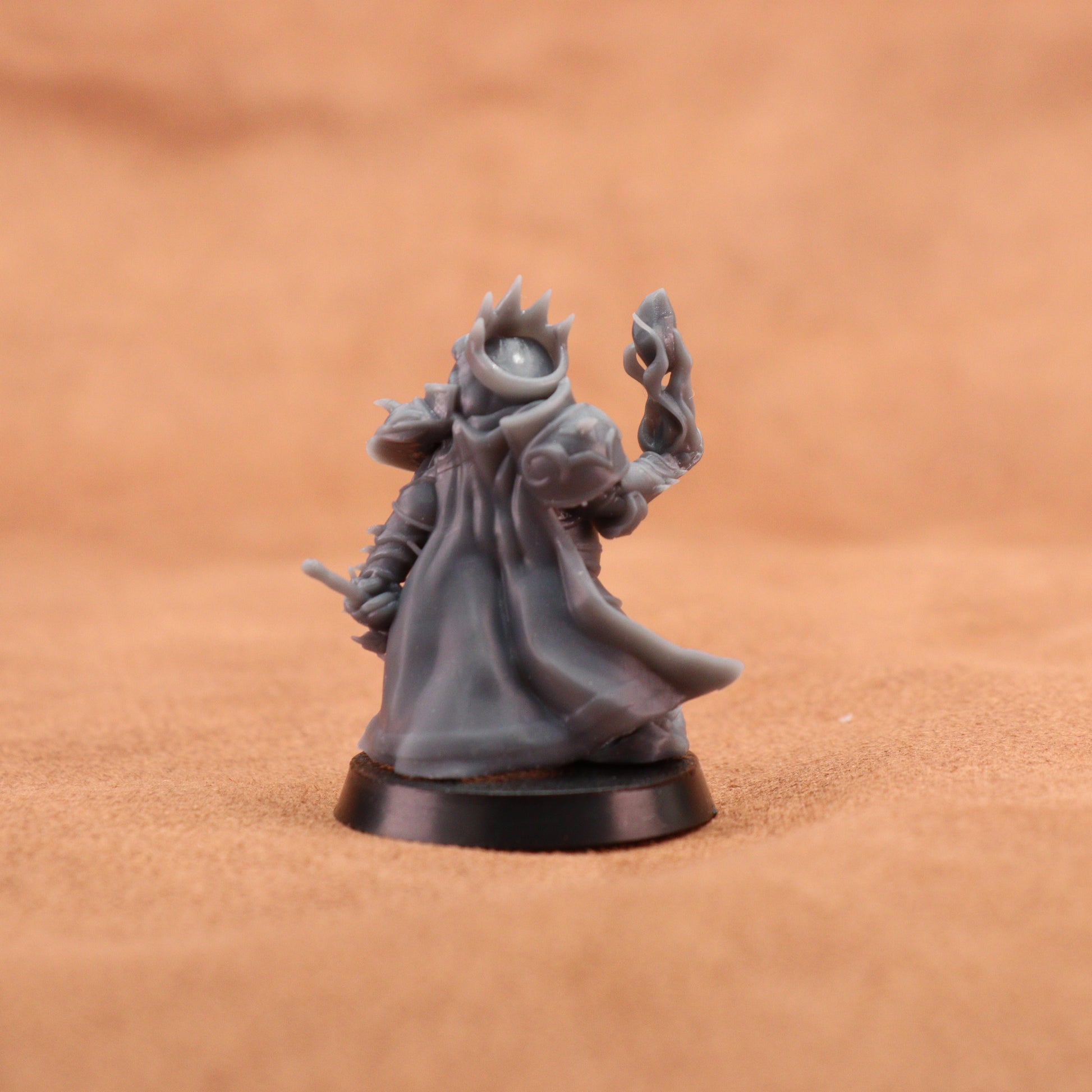 A small unpainted gray fantasy tabletop miniature figurine on a round black base, photographed against a warm tan textured background.
