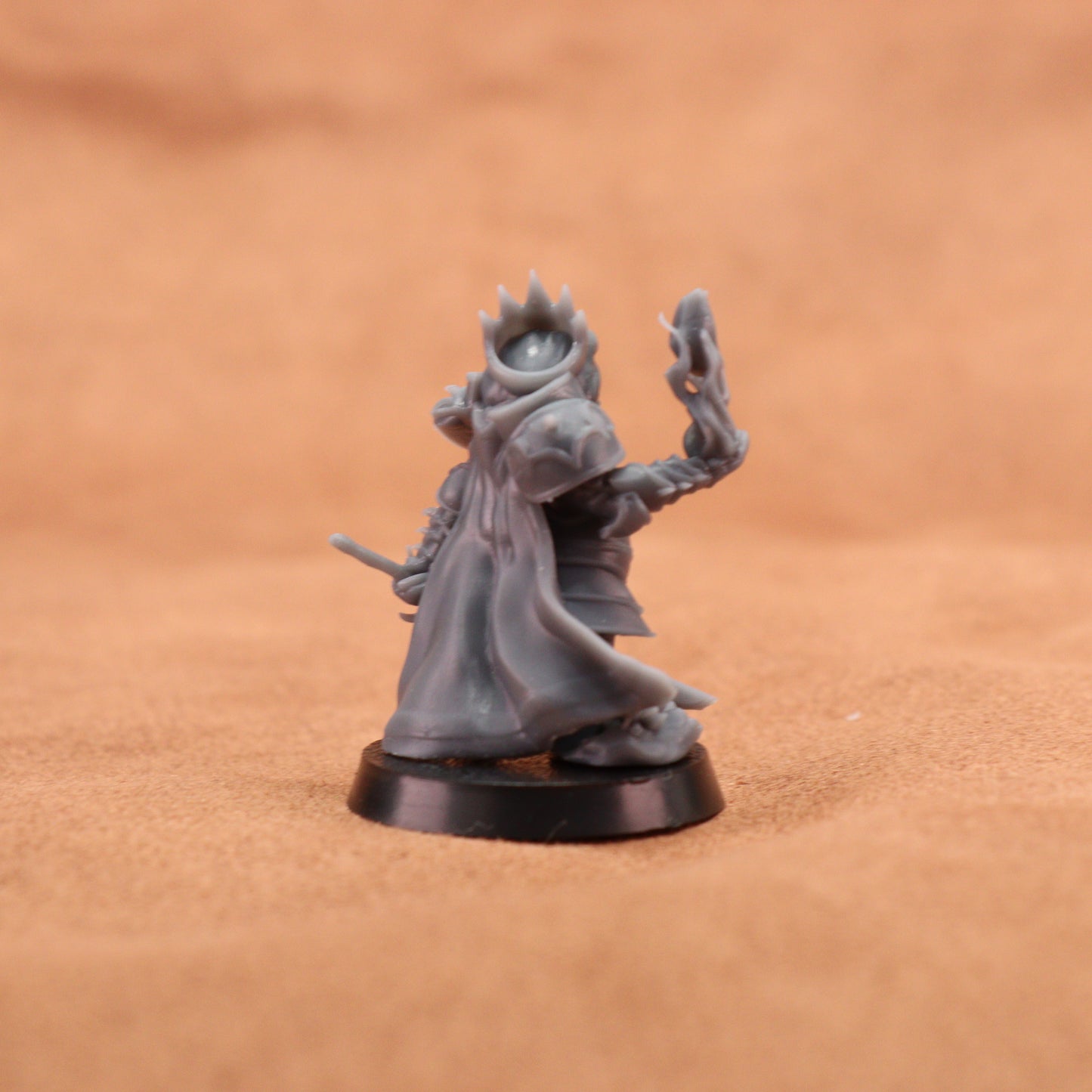 A small unpainted gray fantasy miniature figurine standing on a round black base against a warm brown textured background.
