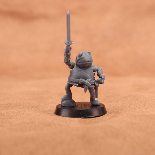 A small unpainted gray fantasy miniature figurine of a warrior holding a sword aloft, standing on a round black base against a warm brown textured background.