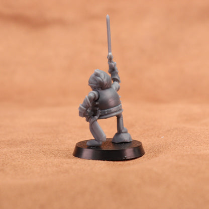 A small unpainted gray fantasy warrior miniature figurine holding a sword aloft, standing on a round black base against a warm brown textured background.