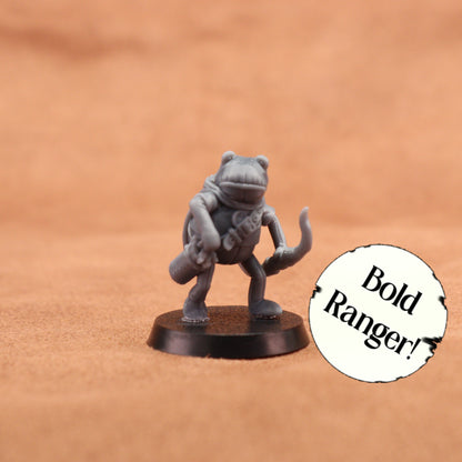 A small unpainted gray fantasy miniature figurine of a frog-like ranger standing on a round black base, photographed against a warm tan textured background. A white circular sticker with the text 'Bold Ranger!' is placed to the right.