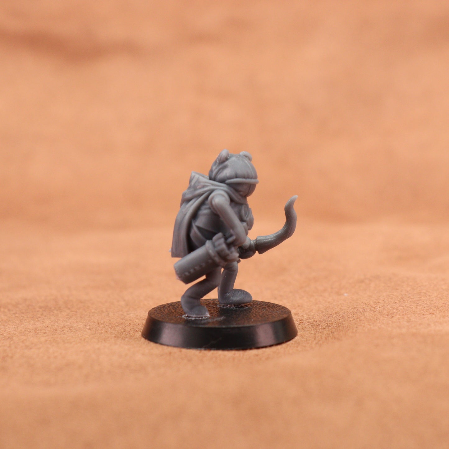 A small gray fantasy miniature figurine of a cat-like character holding a staff, standing on a round black base against a warm brown textured background.