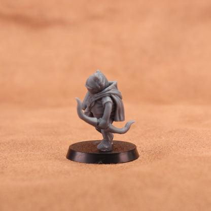 A small unpainted gray fantasy miniature figurine standing on a round black base, photographed against a warm tan textured background.