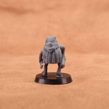A small unpainted gray fantasy miniature figurine of a hooded creature, shown from the back on a round black base against a textured brown background.