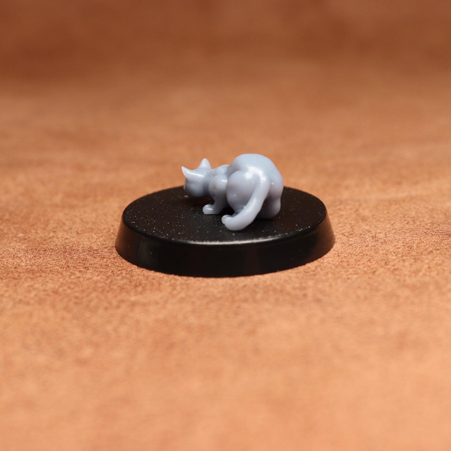 Small gray cat figurine on a black round base against a brown background