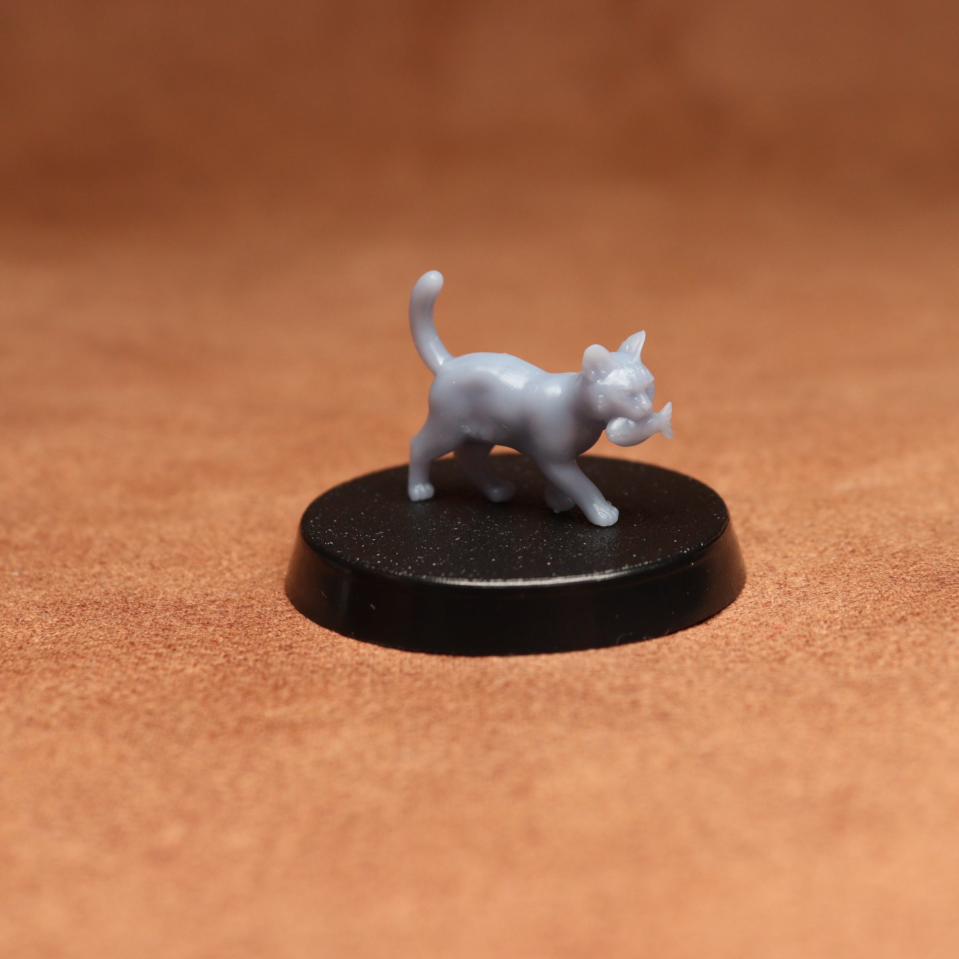 Small gray cat figurine on a black round base against a brown background