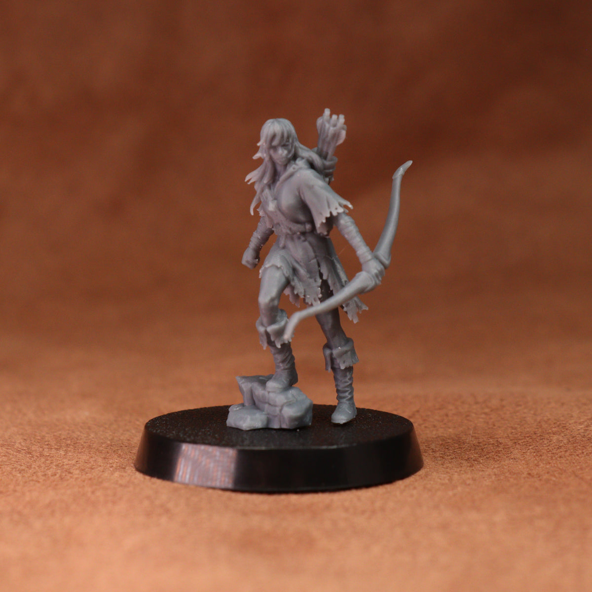 A small unpainted gray fantasy tabletop miniature figurine of a female archer standing on a round black base against a warm brown textured background.