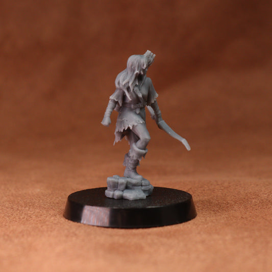 An unpainted gray fantasy miniature figurine of a female warrior holding a sword, standing on a black circular base against a warm brown background.